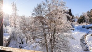 A snowy landscape with a wooden deck and a building in the background. - Studio au Coeur de la Station Morillon 1100! (Morillon)