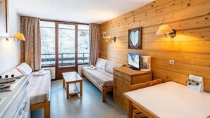 A cozy room with a bed, a desk, a chair, and a table. There is a window with curtains, a wall-mounted lamp, and a picture frame. - Studio au Coeur de la Station Morillon 1100! (Morillon)