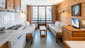 A compact kitchen with wooden cabinets, a stove, and a dining area with benches. - Studio au Coeur de la Station Morillon 1100! (Morillon)