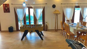 Une pièce comprenant une table de baby-foot, une table à manger avec des chaises, un piano et une lampe.