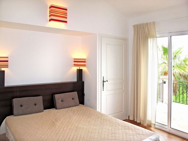 A bedroom with a bed, two bedside lamps, a door, and a balcony with curtains.