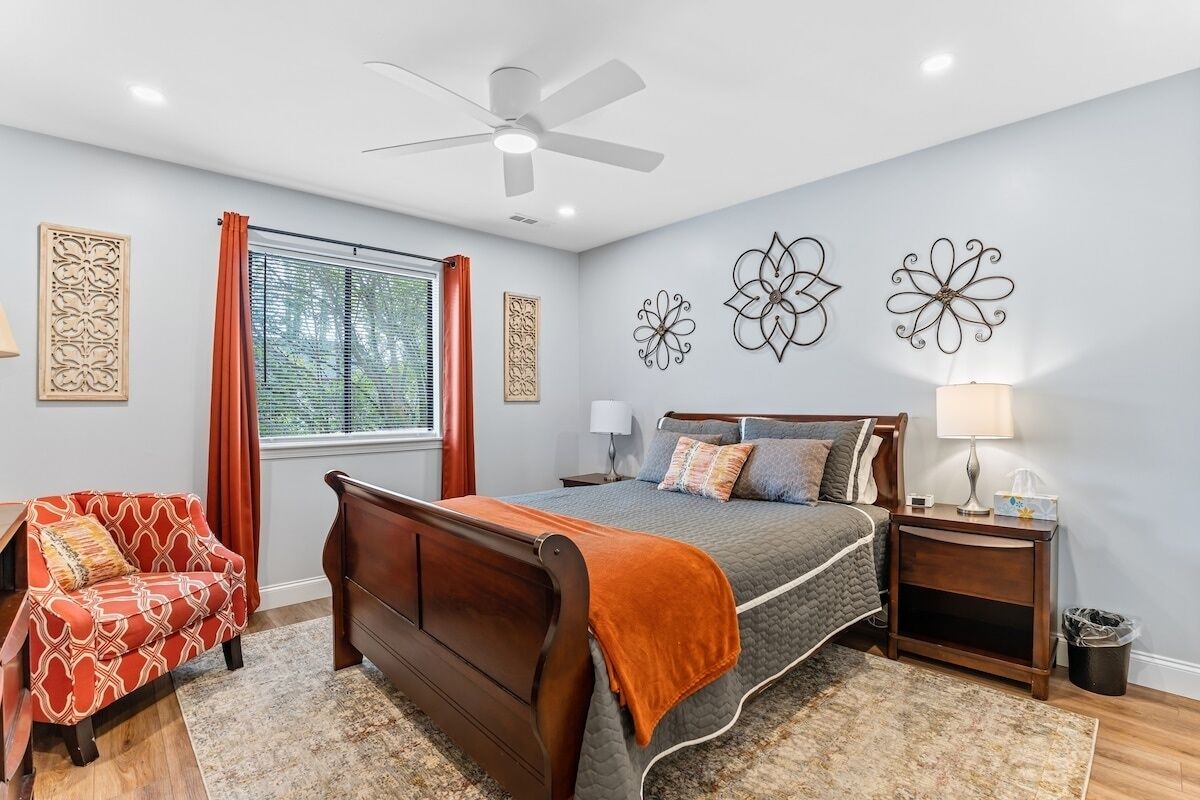 A bedroom with a bed, a nightstand, a chair, a window with curtains, and wall art.