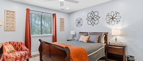 A bedroom with a bed, a nightstand, a chair, a window with curtains, and wall art.
