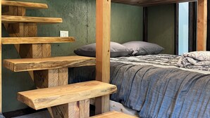 Un letto a castello con una scala in legno e panche, una coperta grigia e un pavimento rivestito di moquette grigia.