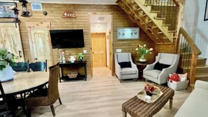 Ein Wohnzimmer mit einer Holztreppe, einem Essbereich mit Tisch und Stühlen sowie zwei Sesseln.