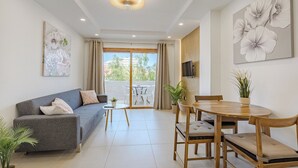 A modern living room with a grey sofa, a wooden dining table with chairs, a small white table, and a large window with curtains.