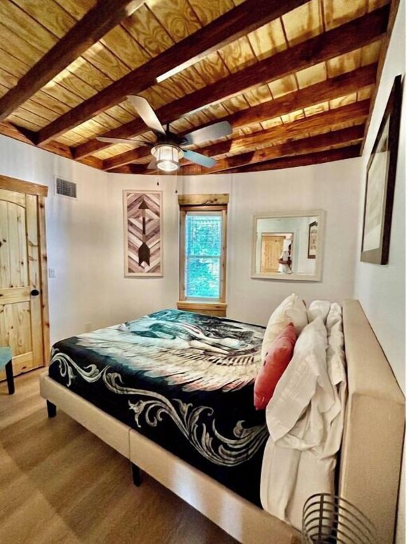 A bedroom with a bed, a ceiling fan, a window, and a door. - Texas Ambience at the Barn and Silo
(Liberty Hill)