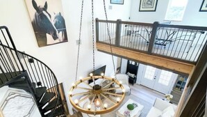A spacious loft with a high ceiling, a spiral staircase, a large chandelier, and a white sofa. - Texas Ambience at the Barn and Silo
 (Liberty Hill)