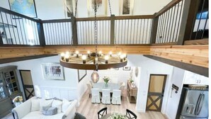 A spacious loft-style living area with a high ceiling, a central chandelier, and a dining area with a round table. - Texas Ambience at the Barn and Silo
 (Liberty Hill)