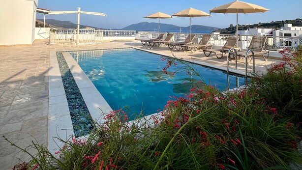A pool area with clear blue water, sun loungers, and umbrellas. - Casa Caria Suites (Bodrum)