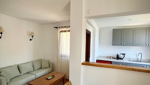 A compact living space with a sofa, a wooden dining table, and a kitchen area with cabinets and a sink. - Casa Caria Suites (Bodrum)