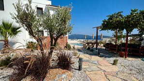 A coastal property with a stone pathway leading to a pool area, surrounded by olive trees and a white building with a red-tiled roof. - Casa Caria Suites (Bodrum)