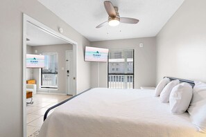 A bedroom with a bed, a ceiling fan, a TV, and a window with blinds.