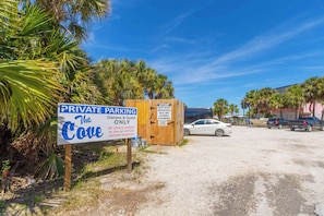 Un espace de stationnement privé, agrémenté d’un panneau indiquant qu’il est réservé aux propriétaires et à leurs invités, une structure en bois avec un panneau, et une voiture blanche garée à l’arrière-plan.
