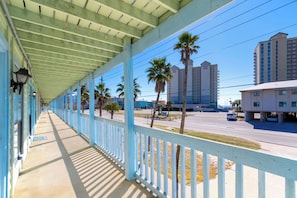 A covered outdoor area with a railing, palm trees, and a road with vehicles in the background.