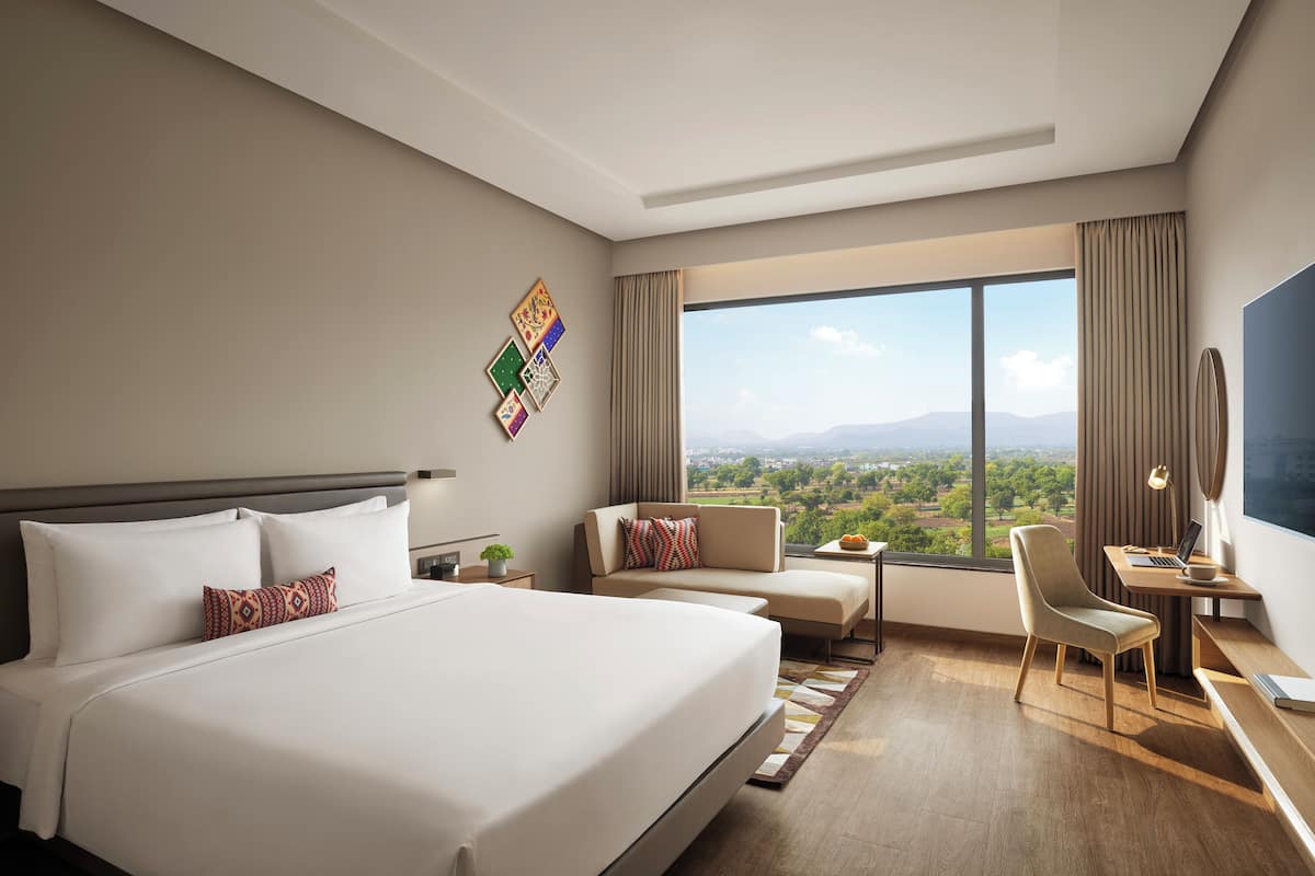 Ein Hotelzimmer mit einem großen Bett, einem Sofa, einem Schreibtisch und Blick auf die Stadt.