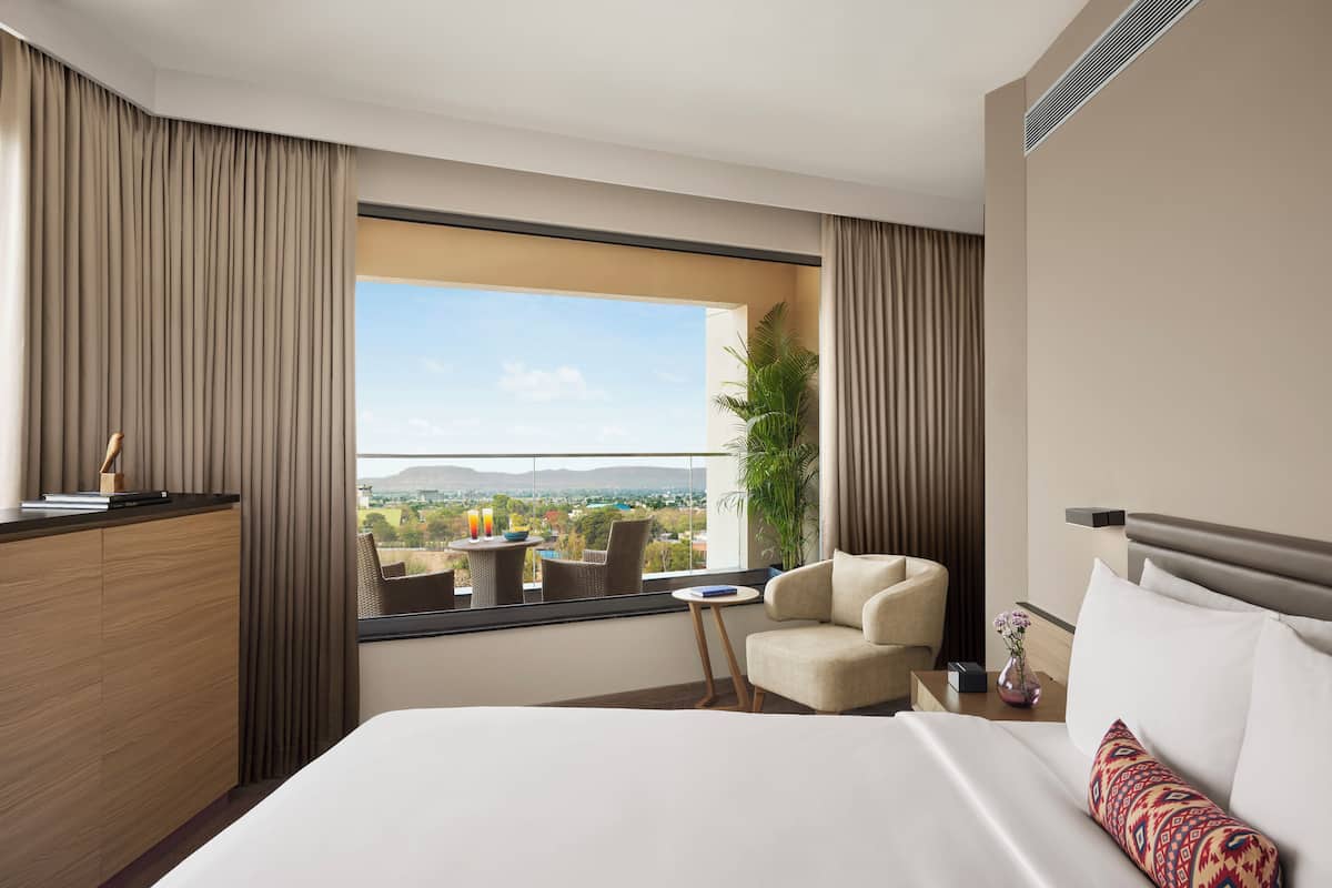 Ein Hotelzimmer mit Bett, Stuhl, kleinem Tisch und Blick ins Freie.