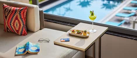 Una habitación acogedora con sofá, una mesita con bebidas y aperitivos, y vista a una piscina.