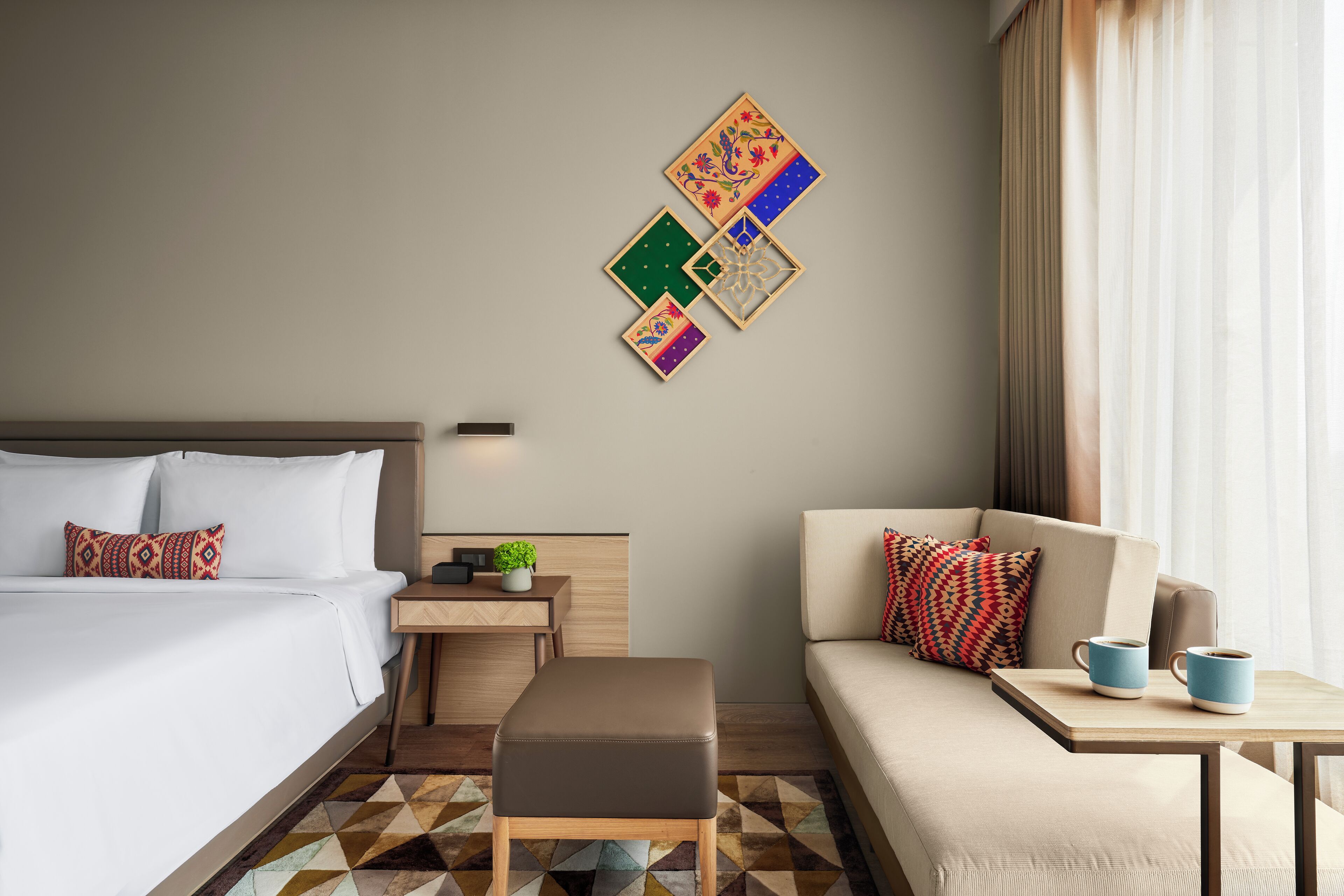 Een hotelkamer met een bed, een bank, een kleintje tafeltje met twee mokken en een muur met decoratieve panelen.