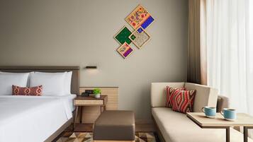 A hotel room with a bed, a sofa, a small table with two mugs, and a wall with decorative panels.