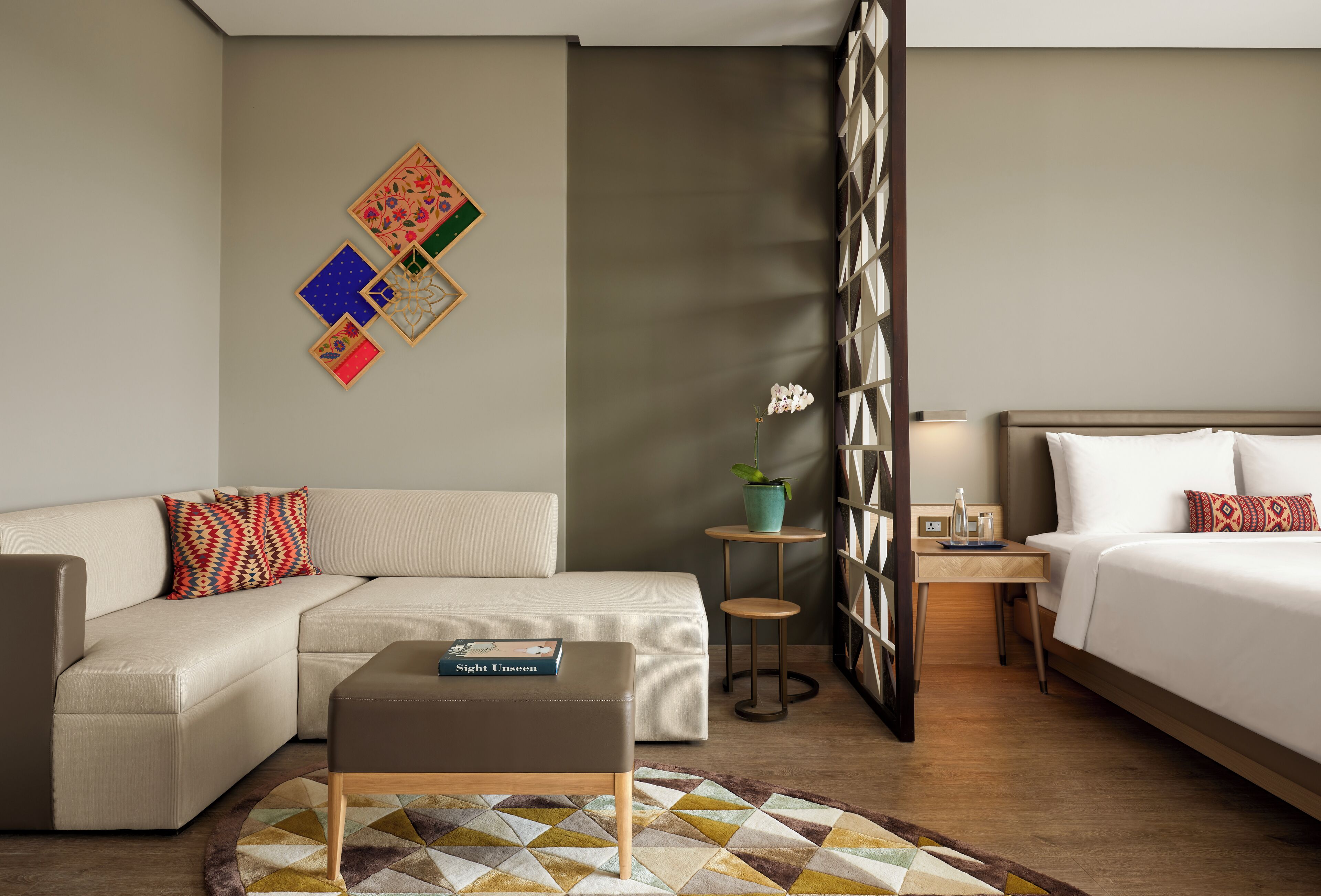 A modern hotel room with a sofa, a bed, a small table, and a decorative wall piece.