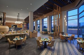 Ein modernes Restaurant mit einer zentralen Bar, mehreren Speisetischen und großen Fenstern mit Blick auf die Stadt.