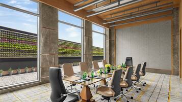 Een moderne vergaderzaal met een grote tafel, meerdere stoelen en uitzicht op een dakmoestuin door grote ramen.