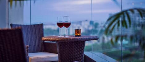A balcony with wicker furniture and two glasses of red wine.
