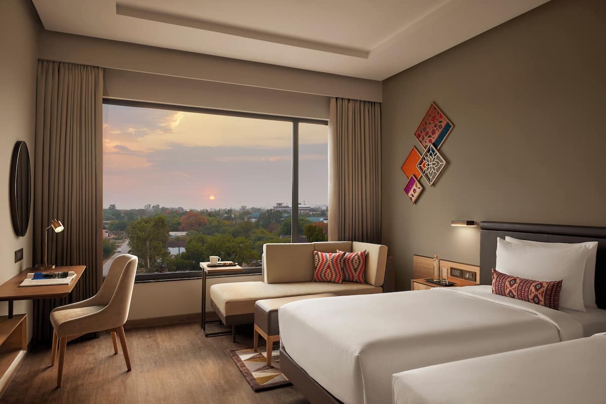 Ein Hotelzimmer mit großem Fenster, Schreibtisch, einer Couch und zwei Betten.