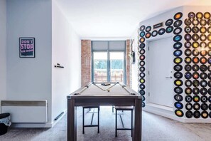 Uma mesa de bilhar em um espaço com uma parede de discos de vinil, uma porta e uma janela.