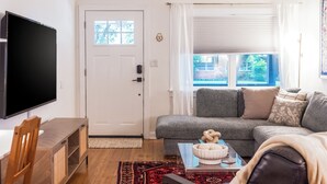 Un salon avec un téléviseur à écran plat, un canapé gris, une table à manger en bois et un tapis rouge à motifs.