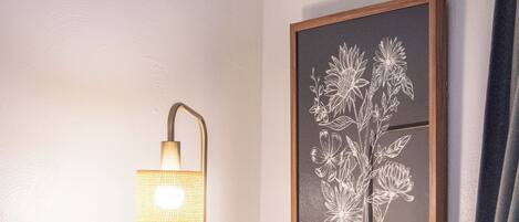 A bedroom with a bed, a bedside lamp, a framed floral artwork, and a curtain.