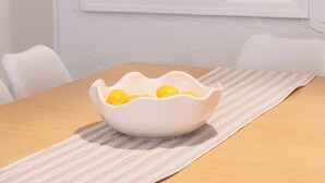 Un coin repas avec une table blanche, un bol de citrons et une plante en macramé suspendue.