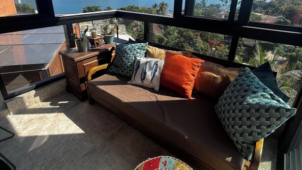 A balcony with a sofa, cushions, a hanging light fixture, and a view of a body of water and mountains. - Recanto à Beira-mar (Ilha Bela)