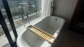 A bathroom with a bathtub, a window with a view of a cityscape, and a textured wall. - Recanto à Beira-mar (Ilha Bela)