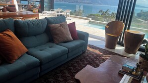 A modern living room with a blue sofa, a patterned rug, and a view of a pool and mountains. - Recanto à Beira-mar (Ilha Bela)