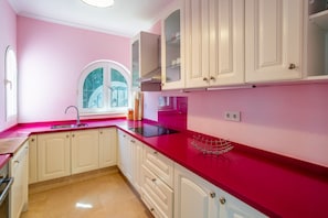 Una cocina con armarios blancos, encimera roja y ventana con vistas.