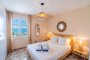 Une chambre d’hôtel avec un lit, une fenêtre donnant sur un paysage agréable, un miroir et un luminaire fixé au mur.