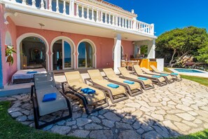 Un complex turístic amb zona de relaxació a la piscina, menjador i vistes al mar.