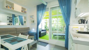 A modern kitchen with white cabinets, a dining table with blue placemats, and a view of a green garden through the window. - Cubo’s Poseidon Suites 3 & Pool for Adults / room / air conditioning / community pool / free wifi (Benalmádena)