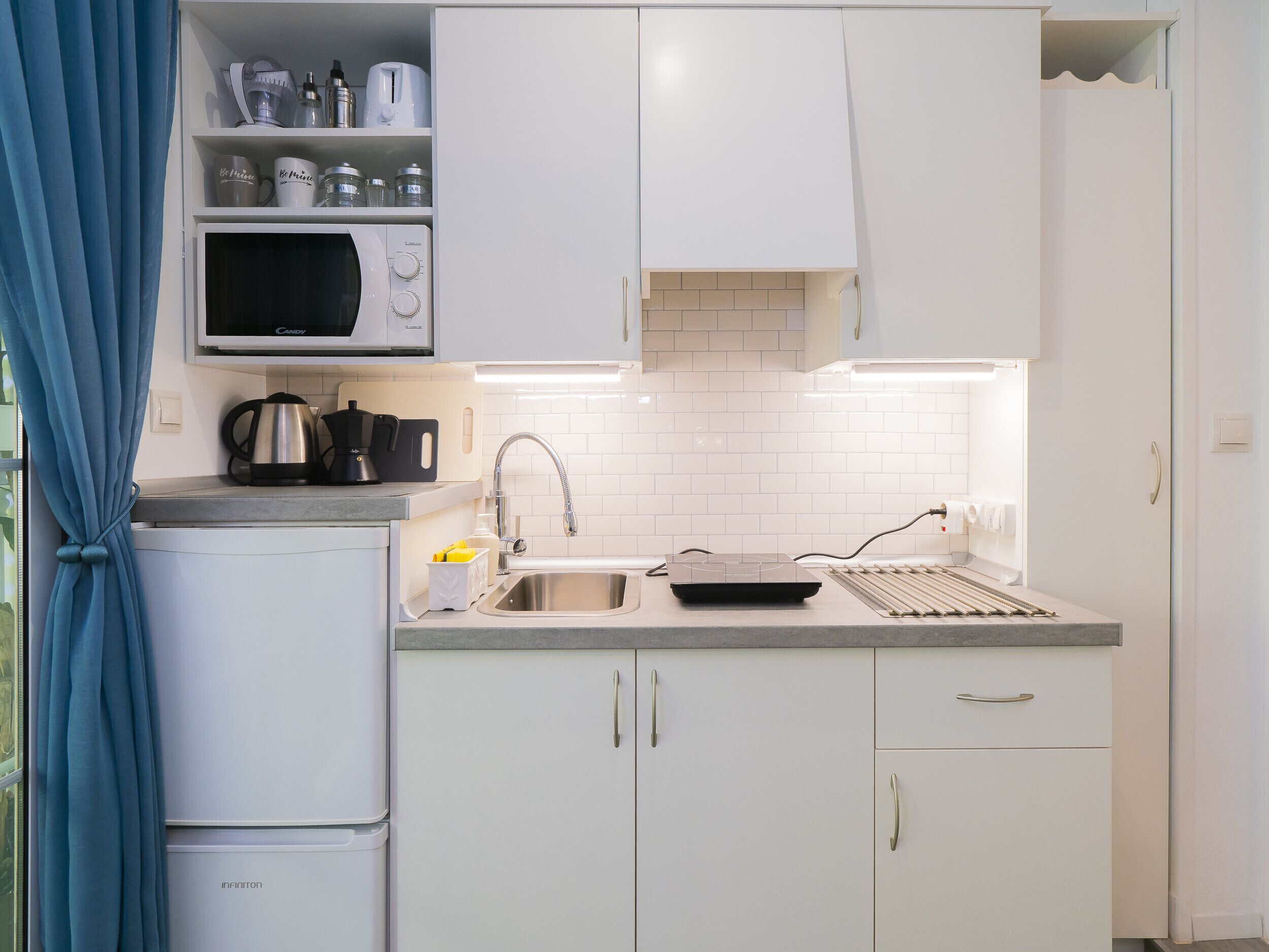 Una cocina compacta con microondas, hervidor, cafetera en la encimera, un lavamanos con grifo y horno tostador.