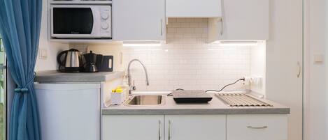 Una cocina compacta con microondas, hervidor, cafetera en la encimera, un lavamanos con grifo y horno tostador.