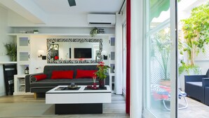 Una sala de estar moderna con un sofá negro, cojines rojos, una mesa de centro blanca y un ventilador de techo.