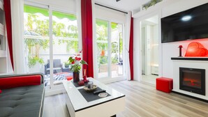 Una sala de estar moderna con un sofá, una mesa de centro y una chimenea. Hay un televisor montado en la pared y un ventilador de techo.