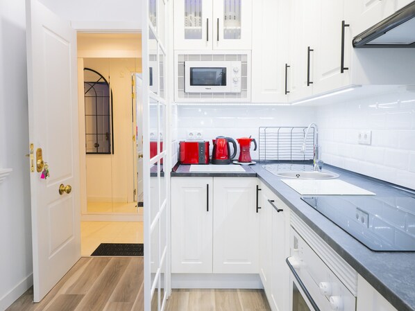 A modern kitchen with white cabinets, a microwave, a red kettle, and a sink.