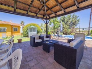 Eine Außenpatio mit Korbmöbeln, einem überdachten Bereich und einem Swimmingpool im Hintergrund.