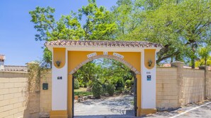 Een toegangspoort met de borden 'FINCA' en 'ALDABA', die uitkomt op een geplaveid pad en groen.