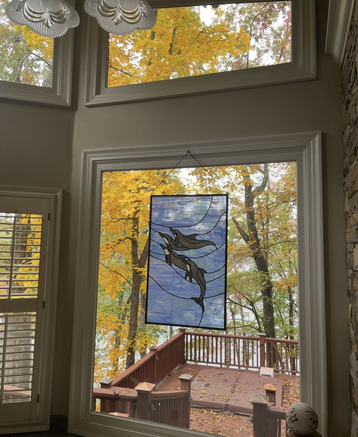 Ein Zimmer mit großem Fenster und Blick auf eine Terrasse und Bäume im Herbstlaub.