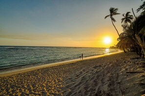 Ein Strand mit Sonnenuntergang, Palmen und Fußabdrücken im Sand.