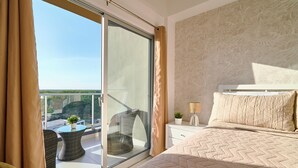 Un dormitorio con una cama grande, una mesita de noche, una lámpara y vistas a un balcón con mobiliario exterior.